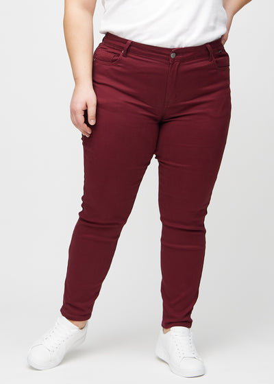 Mørkerøde slim jeans, modelnavn Santas, som sidder tæt til benet, dog lidt løsere ved anklen, på en plus-size model, set forfra.