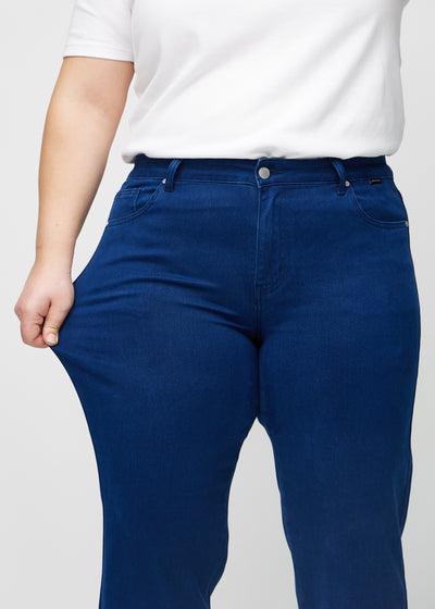 Plus-size model strækker jeansene ved låret for at vise stretch.